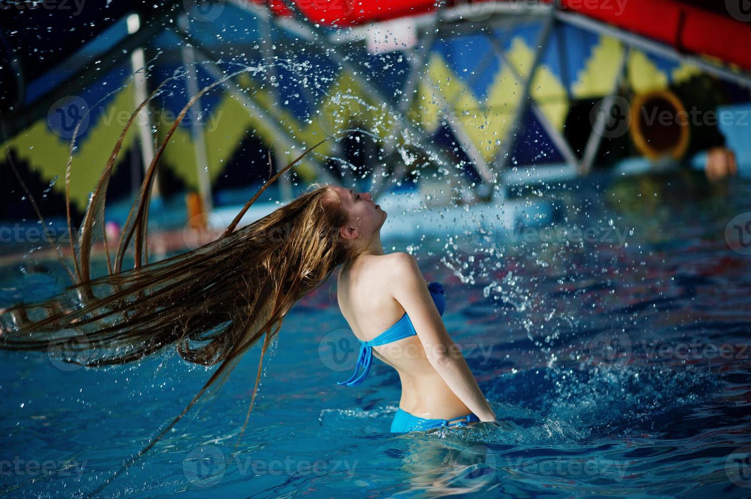 Bewegungseinfrieren auf einem schönen jungen Mädchen, das das Poolwasser mit ihren Haaren im Wasserpark spritzt. foto