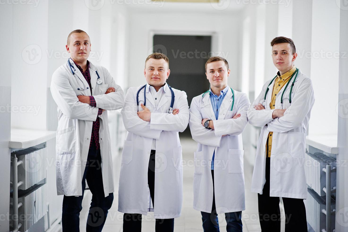 Vier selbstbewusste männliche Ärzte in weißen Kitteln mit Stethoskopen, die im Krankenhaus auf dem Flur stehen. foto