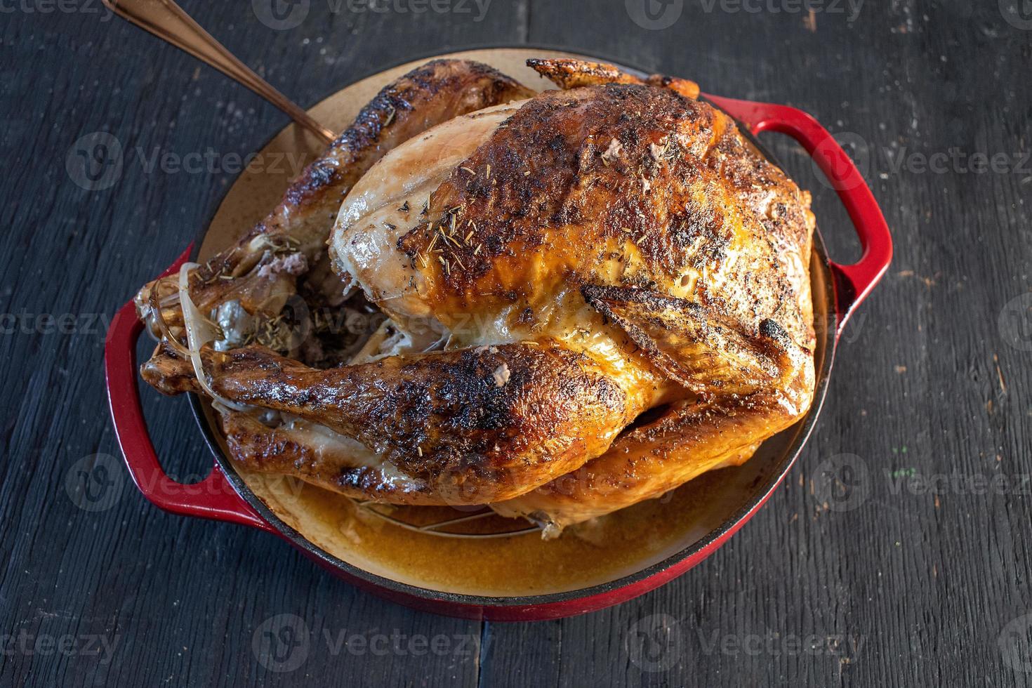 gebackenes ganzes Huhn mit Kräutern in roter Schale auf dunklem Hintergrund foto