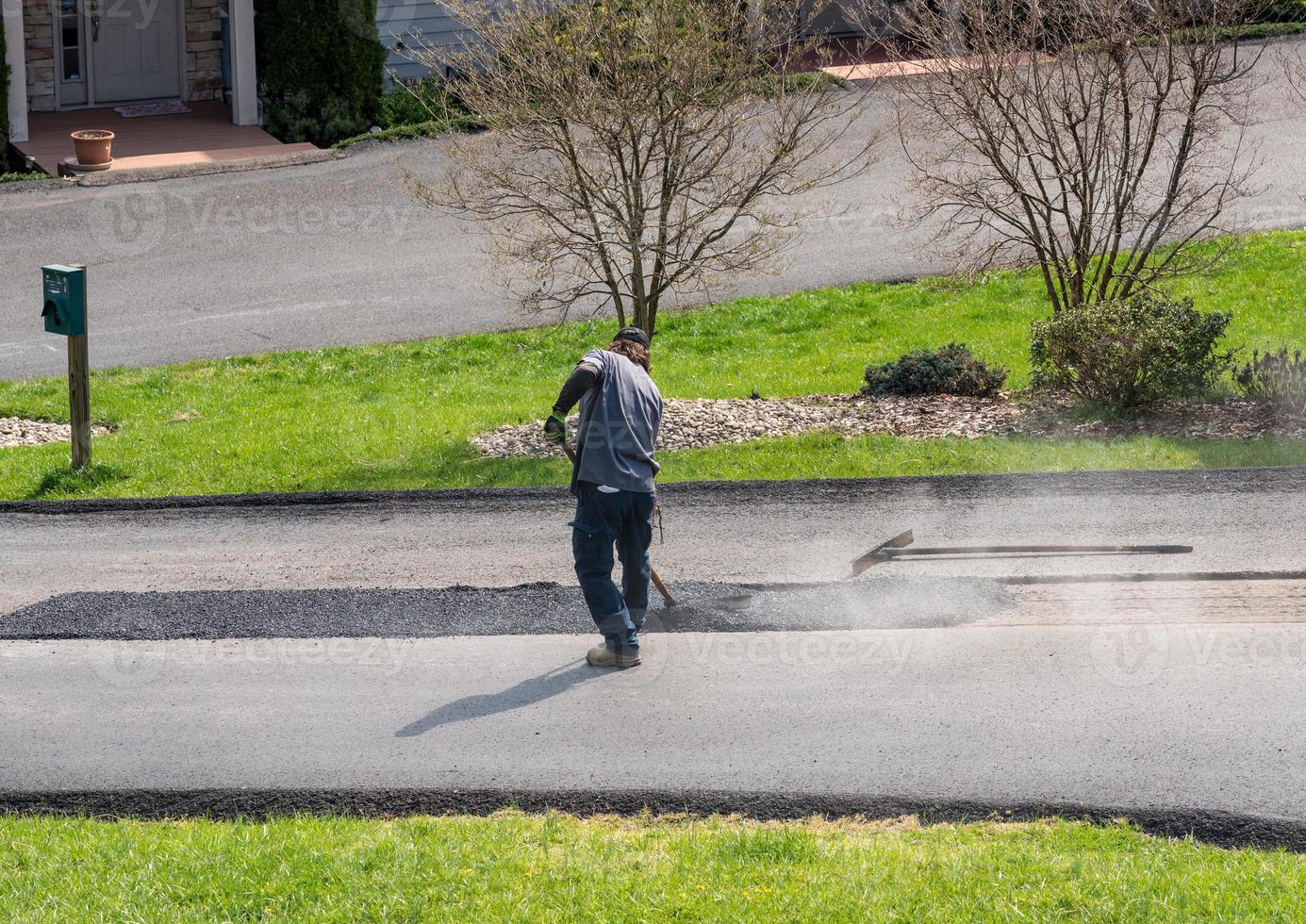 Arbeiter, der eine zusätzliche Asphaltdecke aufträgt, um die Asphaltstraße zu reparieren foto