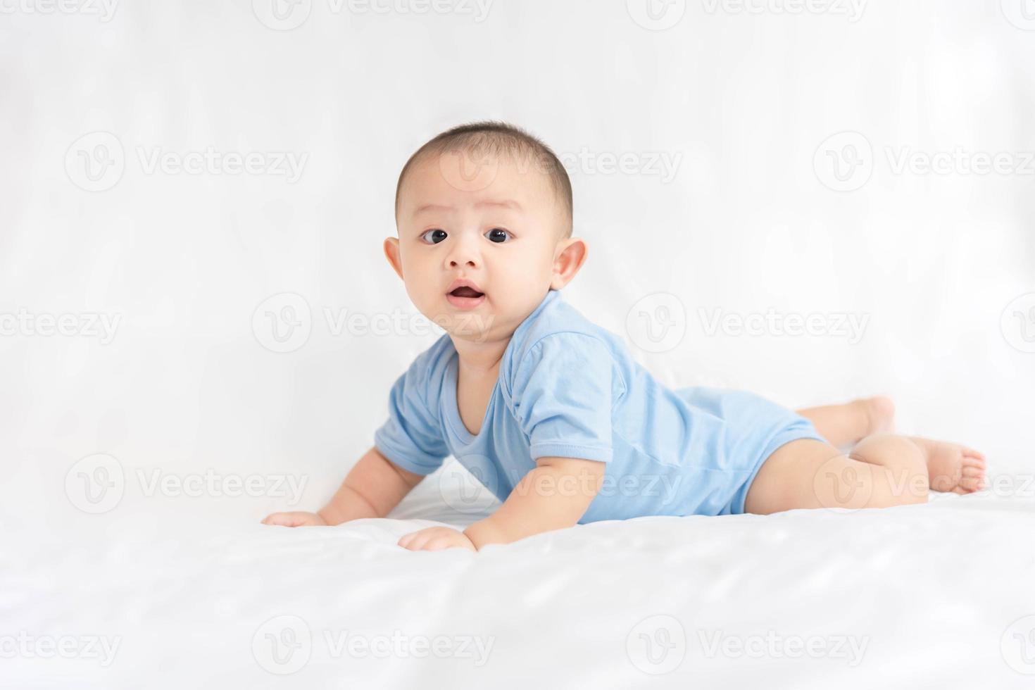 glückliche familie, süßes asiatisches neugeborenes baby tragen blaues hemd liegend, krabbeln, spielen auf weißem bett mit lachendem lächeln glückliches gesicht. Kleines, unschuldiges, entzückendes Kind im ersten Lebenstag. Muttertagskonzept. foto