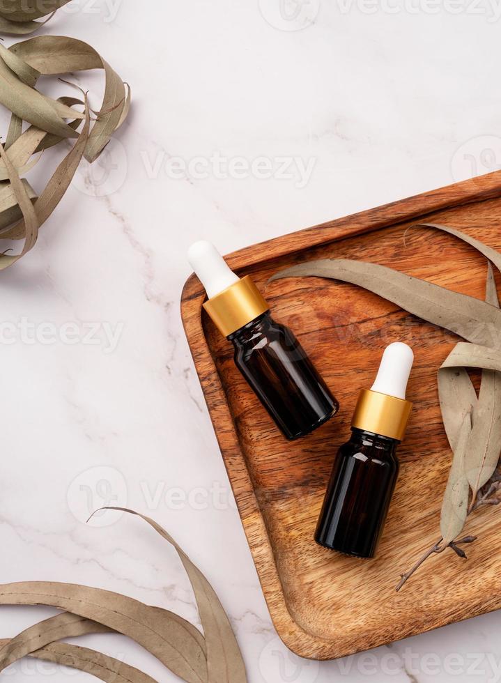 Blick von oben auf die leere Braunglasflasche mit ätherischem Öl und Pipette auf Betongrund mit Eukalyptusblättern foto