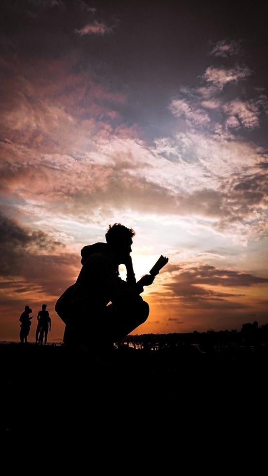 Silhouette eines Mannes, der bei Sonnenuntergang ein Buch liest foto