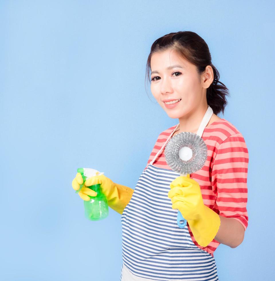 Schöne asiatische Frau, die ein Flaschenspray hält, um das Gerät zu reinigen, und glücklich lächelt, um das Haus zu reinigen foto