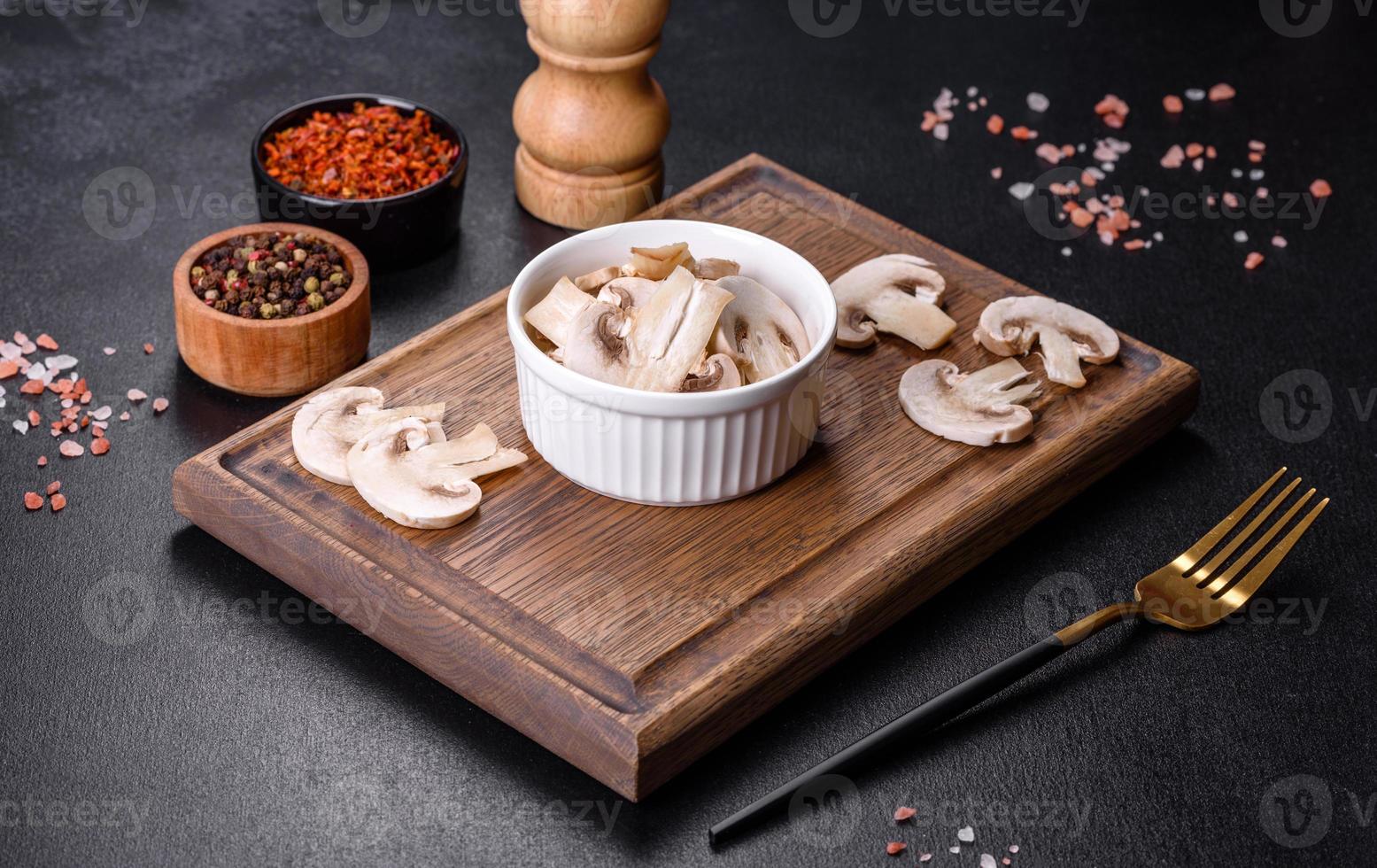 schöne junge weiße champignons, die auf einem dunklen betonhintergrund in scheiben gerissen werden foto