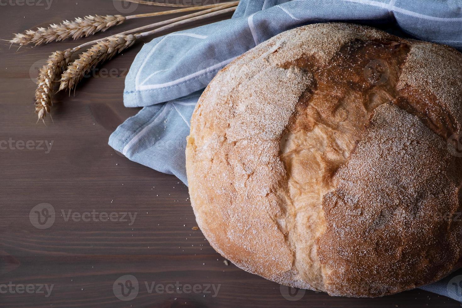 Laib frisch gebackenes hausgemachtes handwerkliches Brot und Ährchen mit Weizenkörnern foto