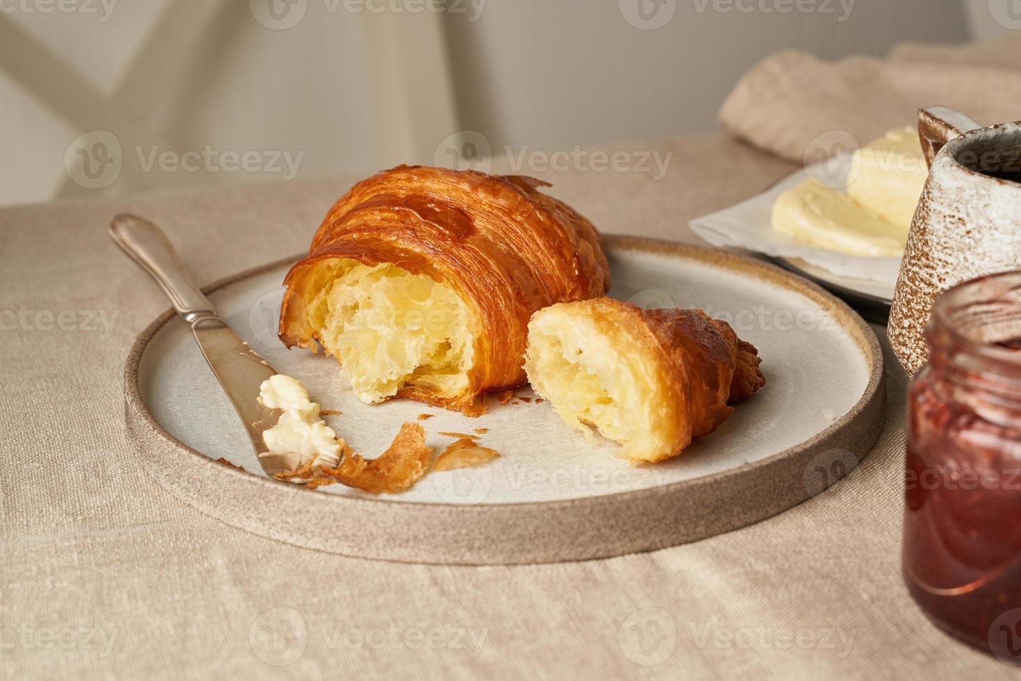 ein leckeres croissant auf dem teller und ein heißes getränk im becher. morgens französisches frühstück foto