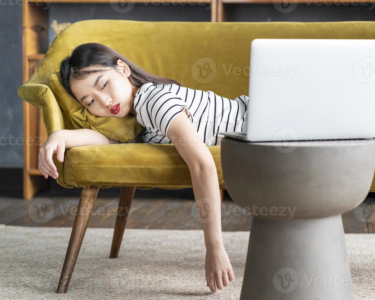 Junges asiatisches Mädchen schlief auf der Couch vor dem Laptop ein. süße gelangweilte frau, die langweiligen film anschaut foto