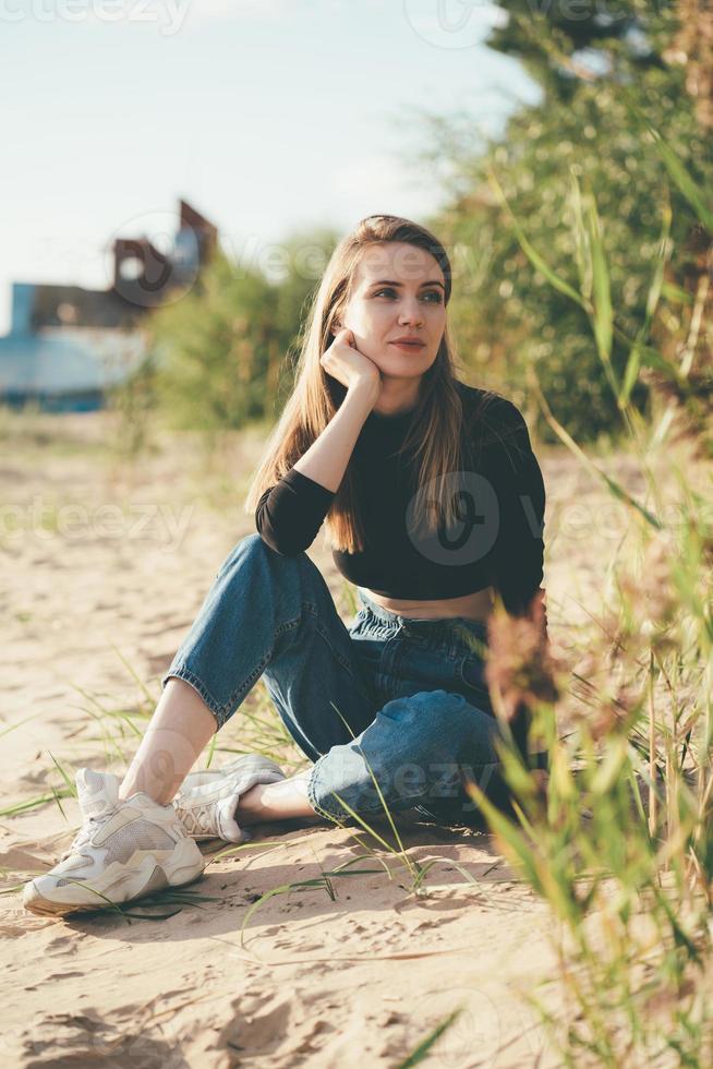 schöne nachdenkliche frau in voller länge, die abends bei sonnenuntergang am strand sitzt. hübsches Weib foto