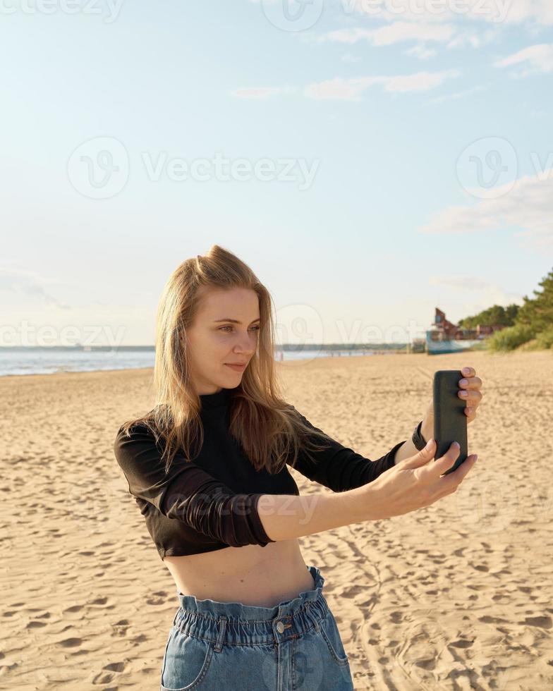schöne frau, die selfie auf ozean- oder meeresküste an einem sonnigen tag macht foto