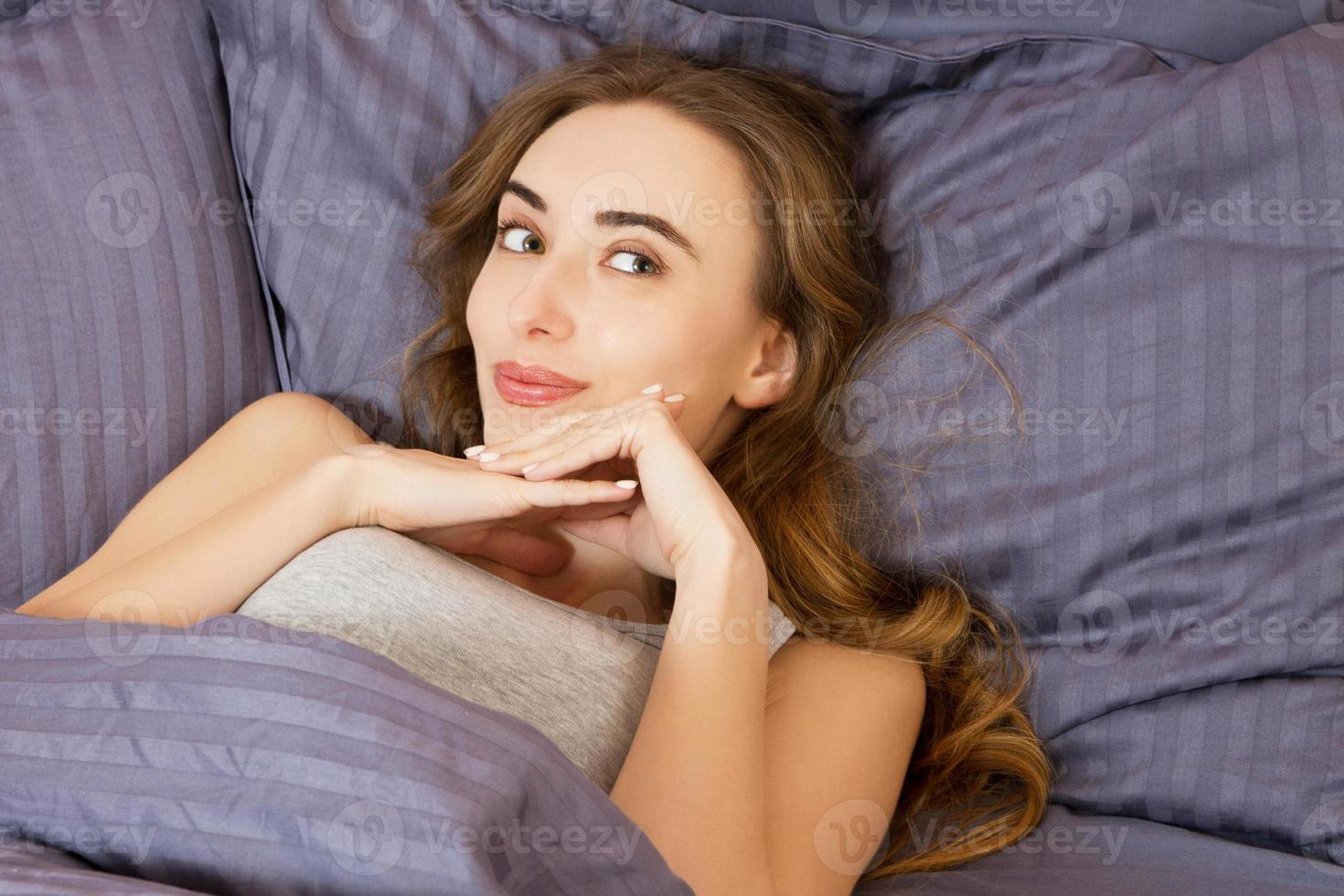 Porträt hübsches junges weißes Mädchen auf dem Bett in einer modernen Wohnung am Morgen. Sie hält die Augen offen und sieht zufrieden aus. schöne junge Frau, die sich morgens im Bett sonnt. schönes Modelgesicht foto