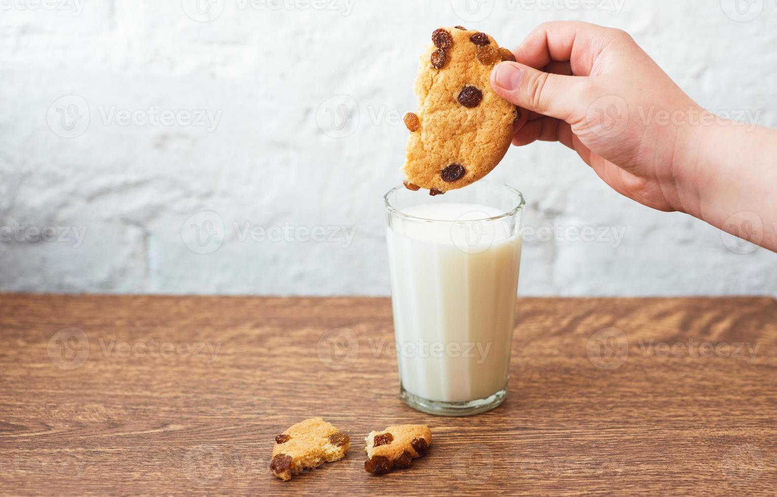 Junge taucht leckeren Keks in ein Glas Milch. duftende, leckere, hausgemachte Kekse mit Rosinen und einem Glas frischer Milch foto