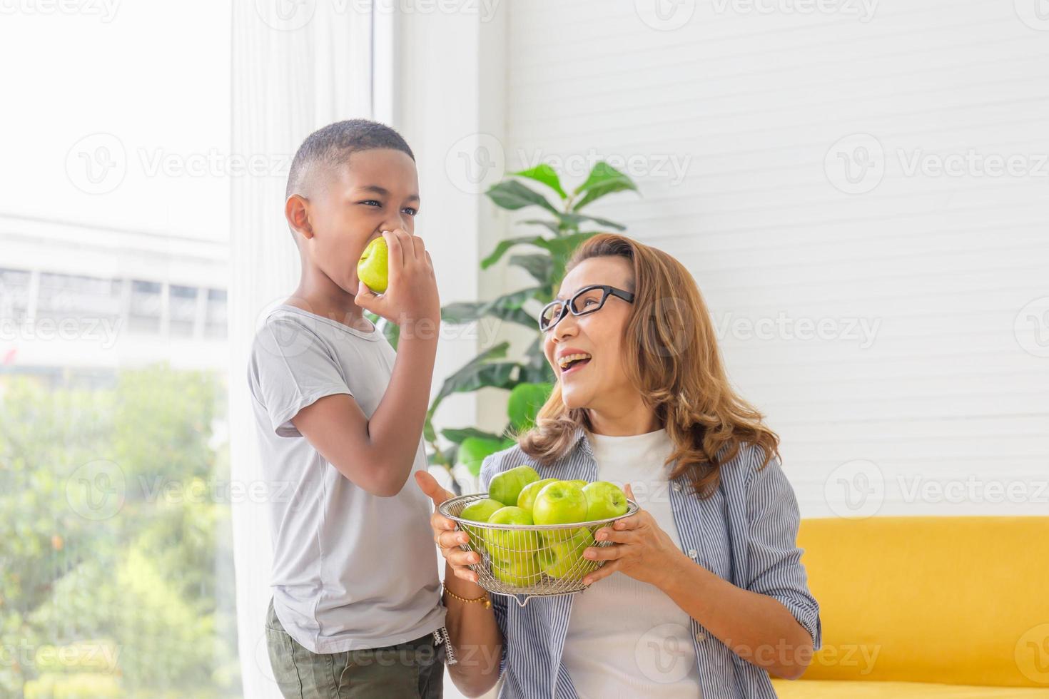 kind isst grüne apfelfrucht, großmutter und enkelkinder mit apfel im wohnzimmer foto