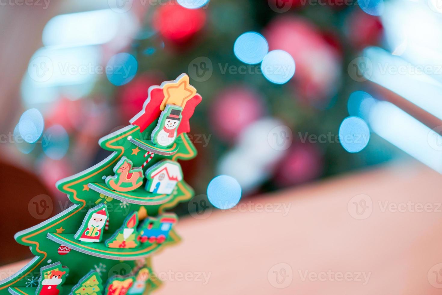 weihnachtsbaumpapierhandwerksdekoration auf dem holztisch mit unschärfe großem weihnachtsbaum hinter sich. foto