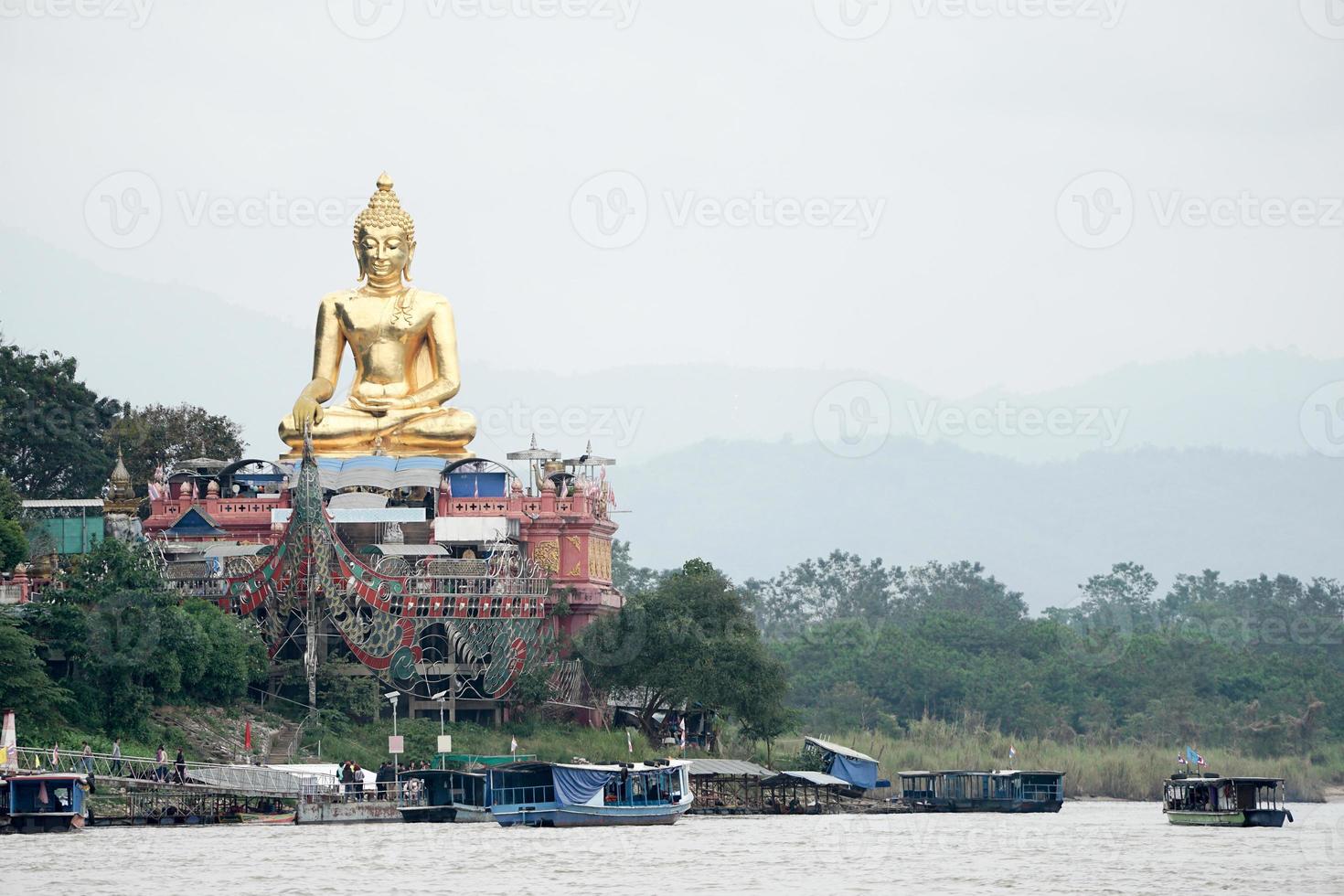 sehr große große goldene buddha-statue, die neben fluss sitzt foto