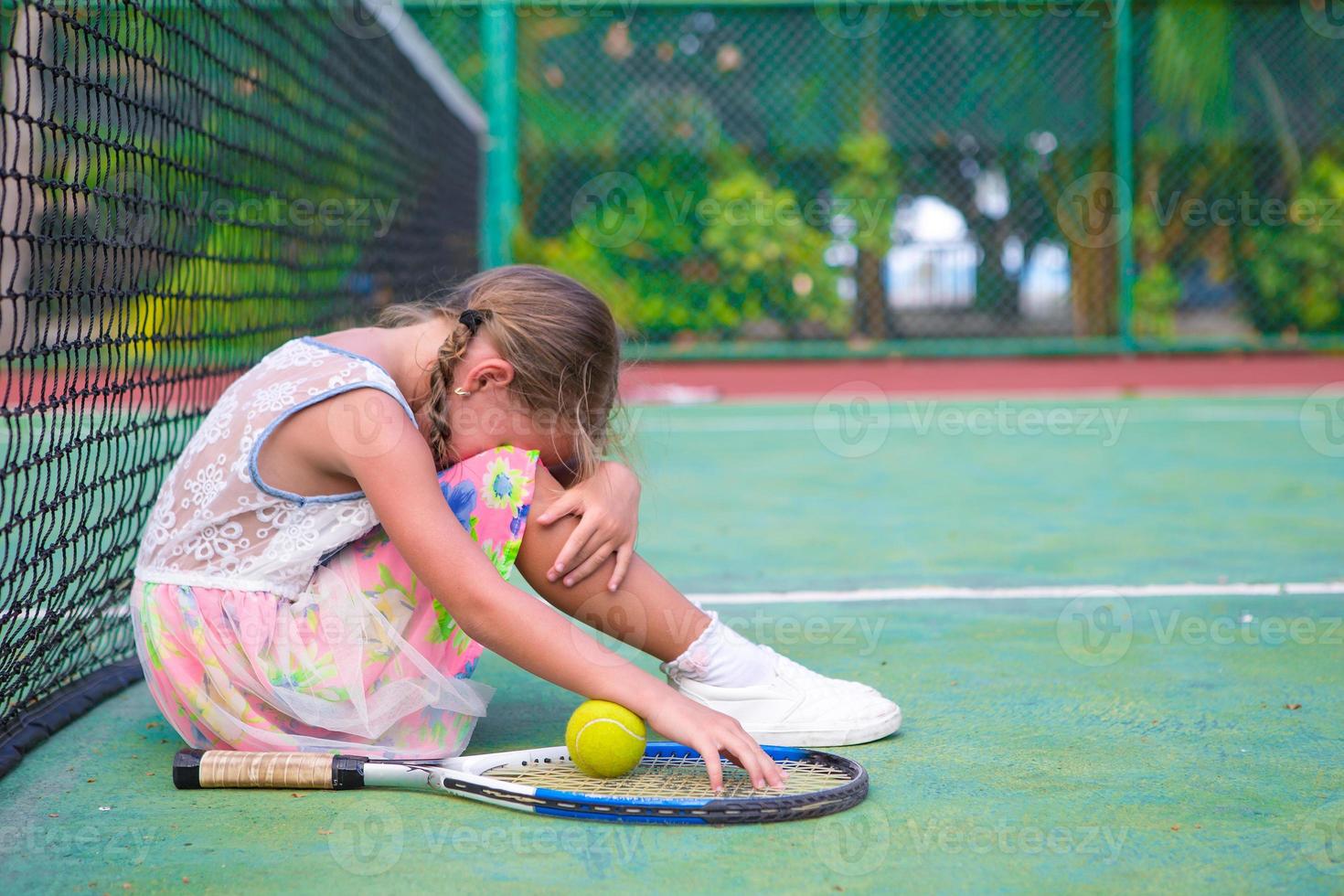 kleines trauriges Mädchen auf dem Tennisplatz foto