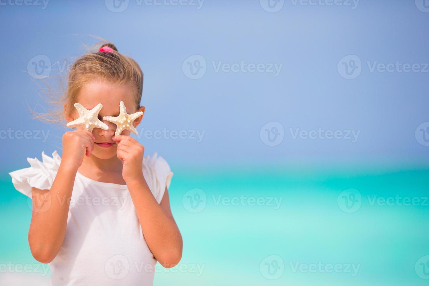 Entzückendes kleines Mädchen mit Seesternen am Strand während der Sommerferien foto