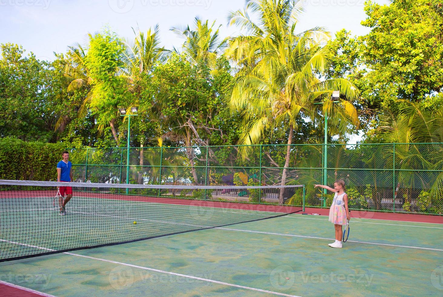 kleines Mädchen, das mit ihrem Vater auf dem Platz Tennis spielt foto