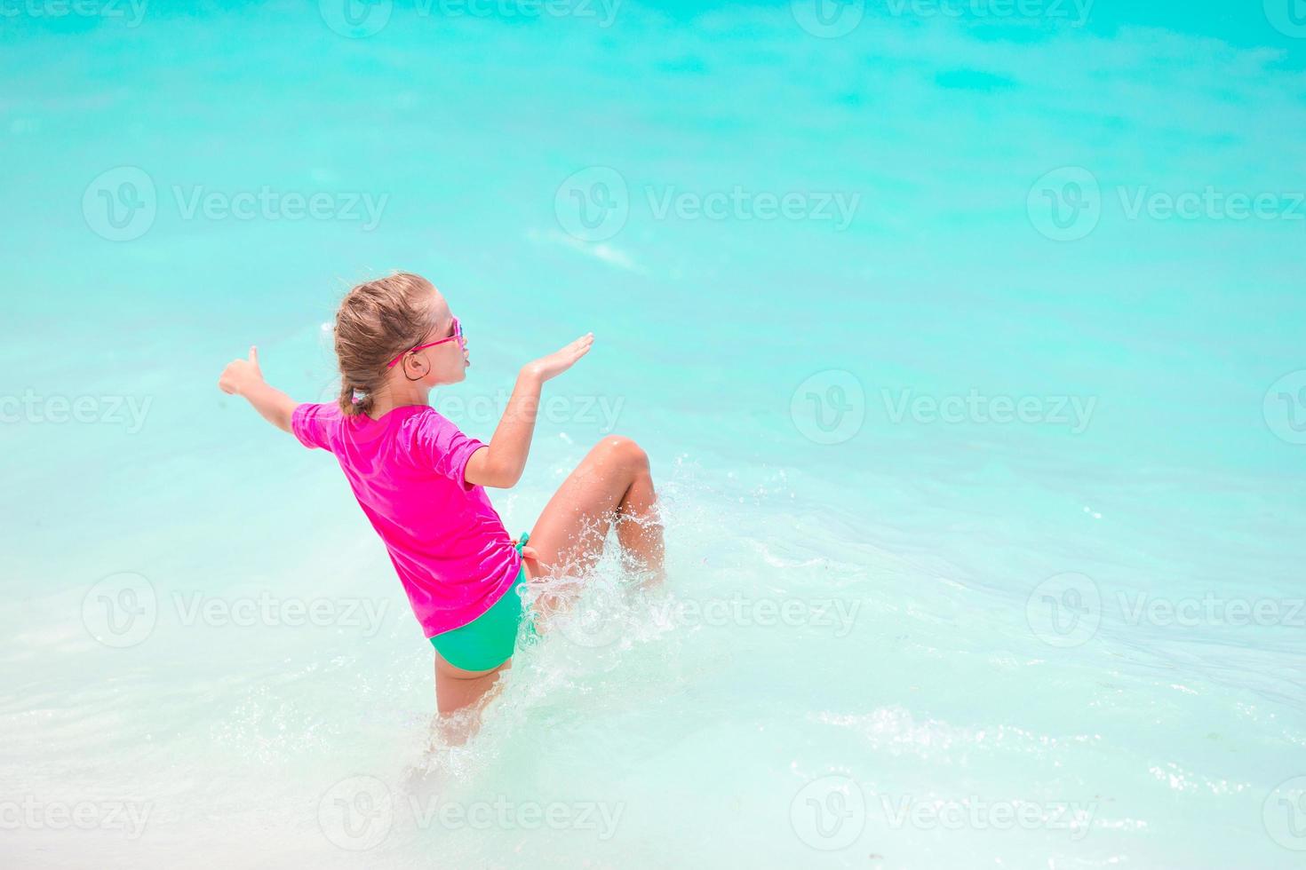 entzückendes kleines Mädchen, das während der Sommerferien im tropischen Flachwasser spritzt foto