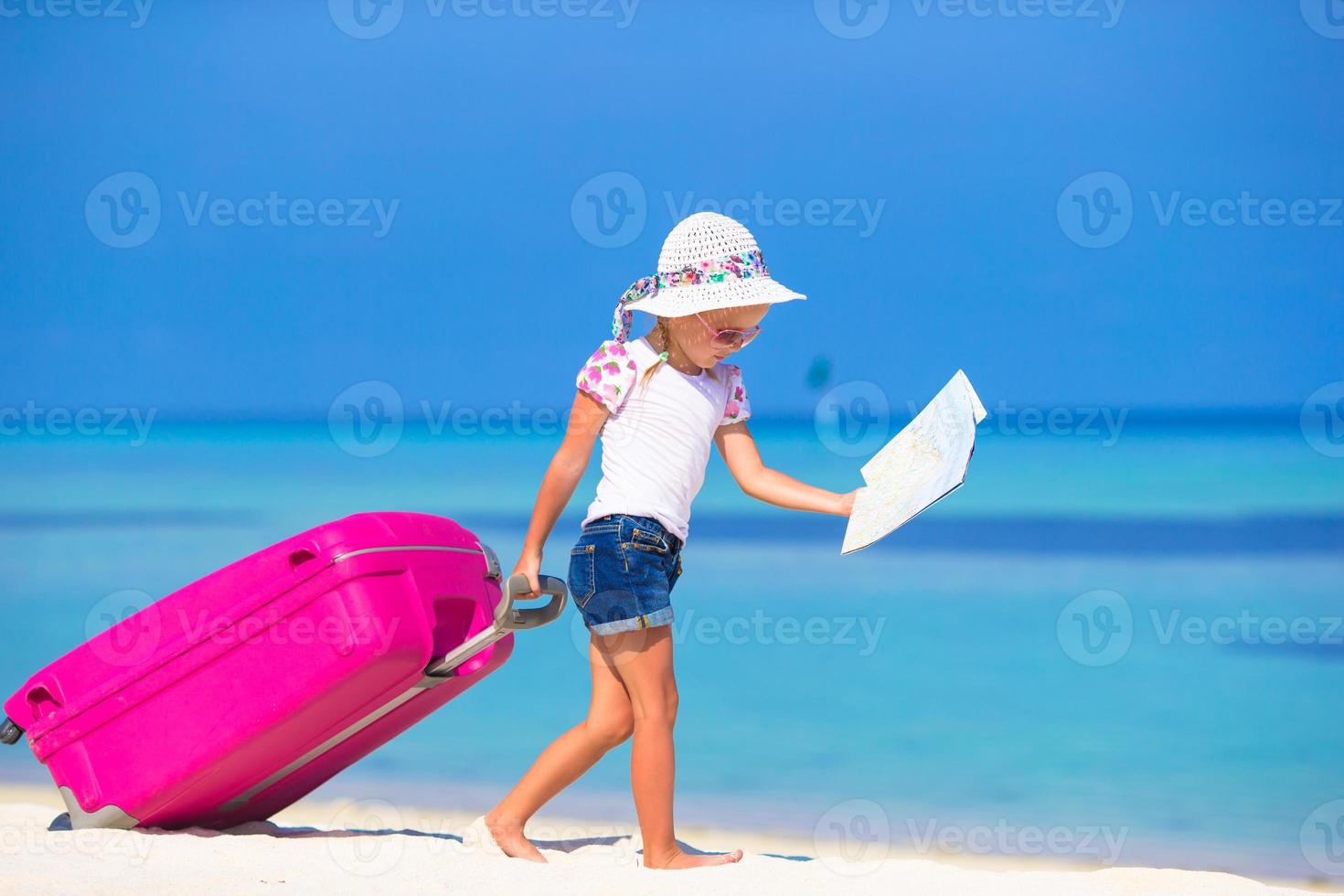 Kleines entzückendes Mädchen mit großem Koffer am tropischen weißen Strand foto