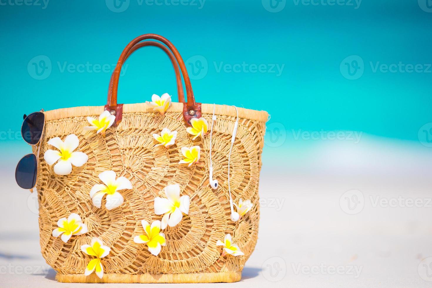 Closeup schöne Tasche mit Frangipani-Blüten und Sonnenbrille am weißen Strand foto