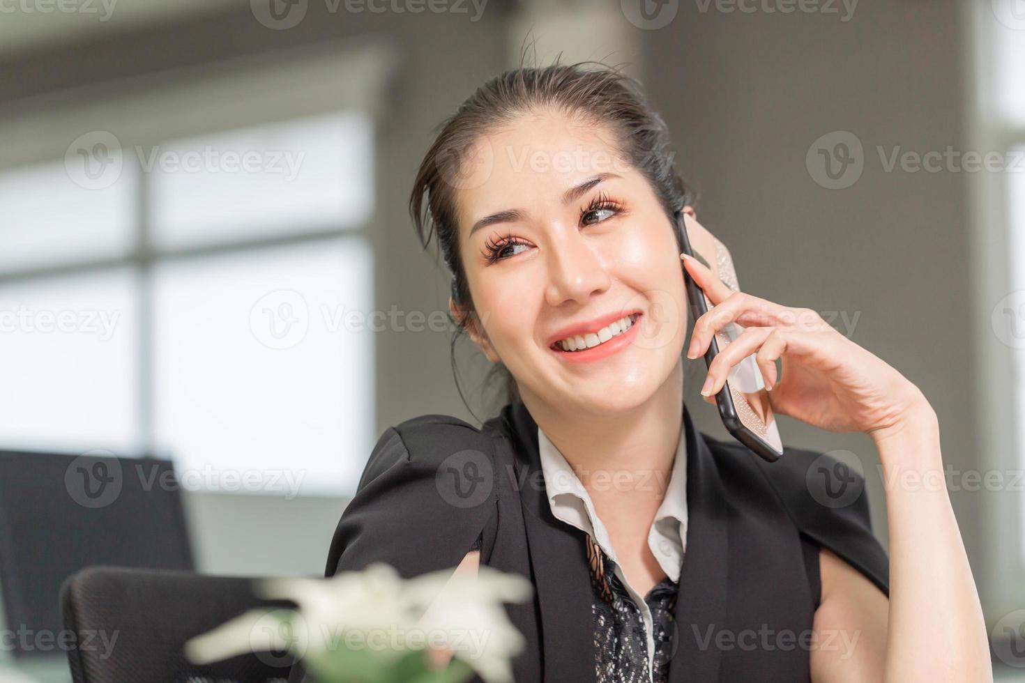 lächelnde Geschäftsfrau mit Telefon im Büro. Aufgeregtes hübsches Mädchen mit Smartphone im Büro, Frau, die in ihrem Heimbüro arbeitet foto