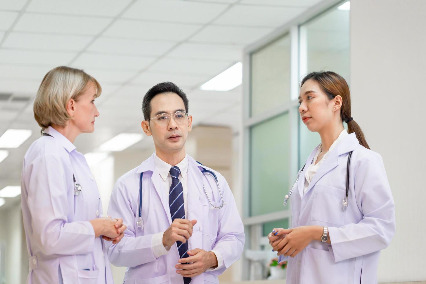 Ärzteteam diskutiert auf dem Korridor im Krankenhaus, Team von Ärzten gemischter Rassen, Gruppe multiethnischer Mediziner, Männer und Frauen, die sich unterhalten und diskutieren foto