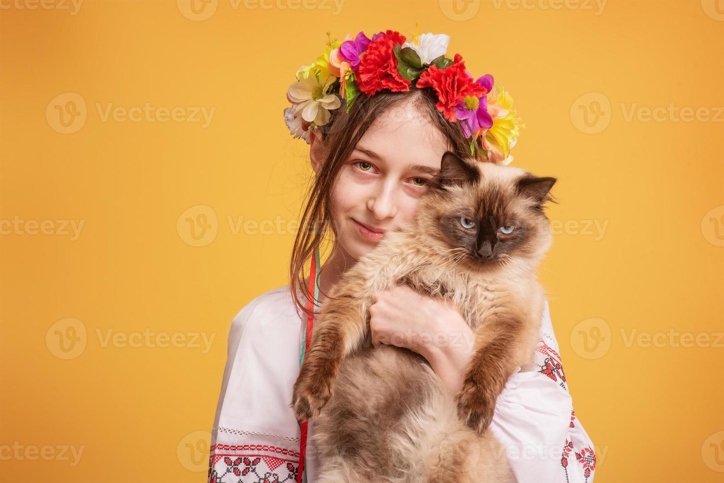 Teenager-Mädchen mit einem Kranz auf dem Kopf und einem bestickten Hemd mit einer Katze im Arm. Haustier. foto