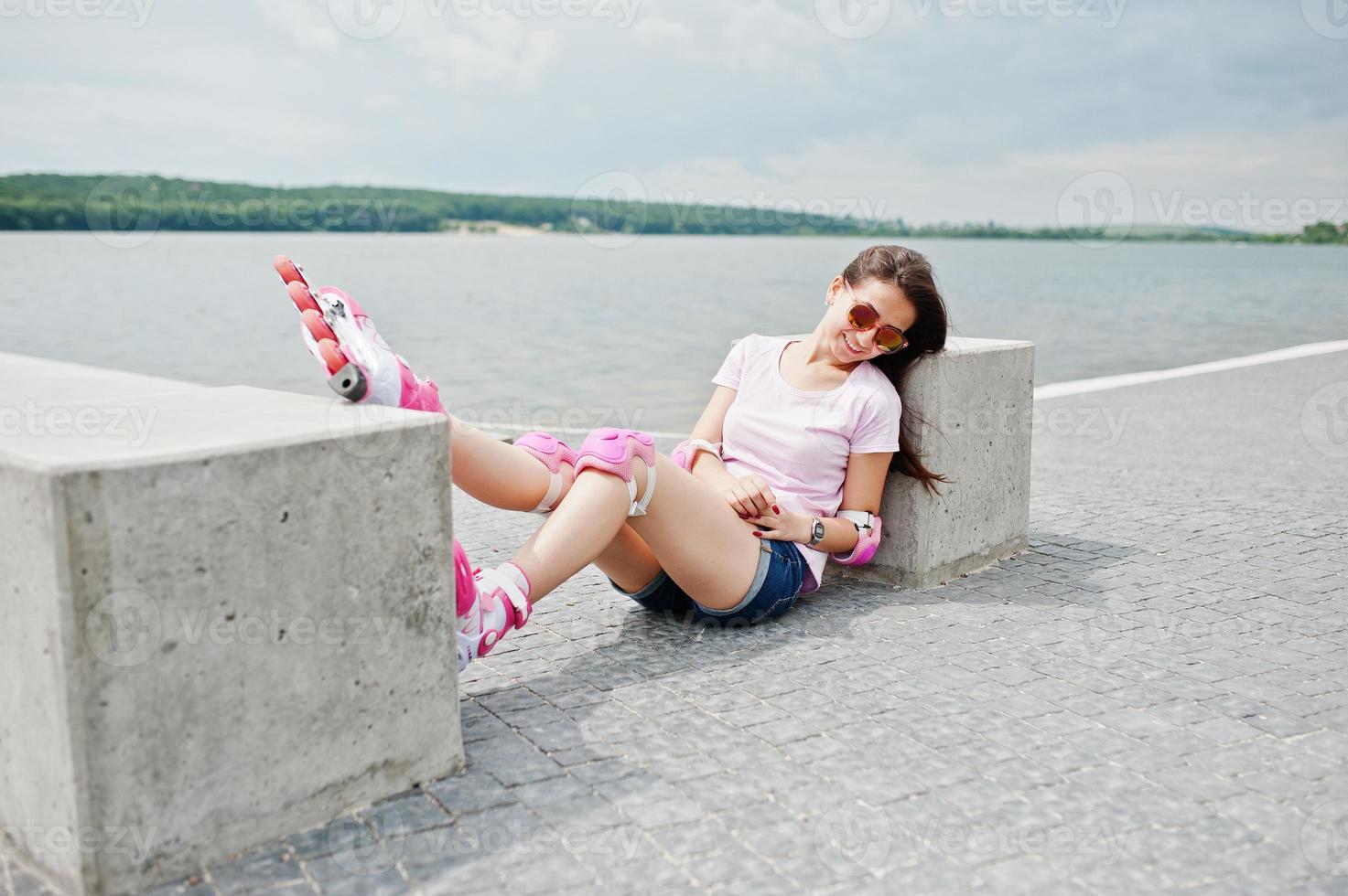 Porträt einer schönen Frau, die neben einem Betonwürfel mit Rollschuhen und Freizeitkleidung auf dem Boden sitzt. foto