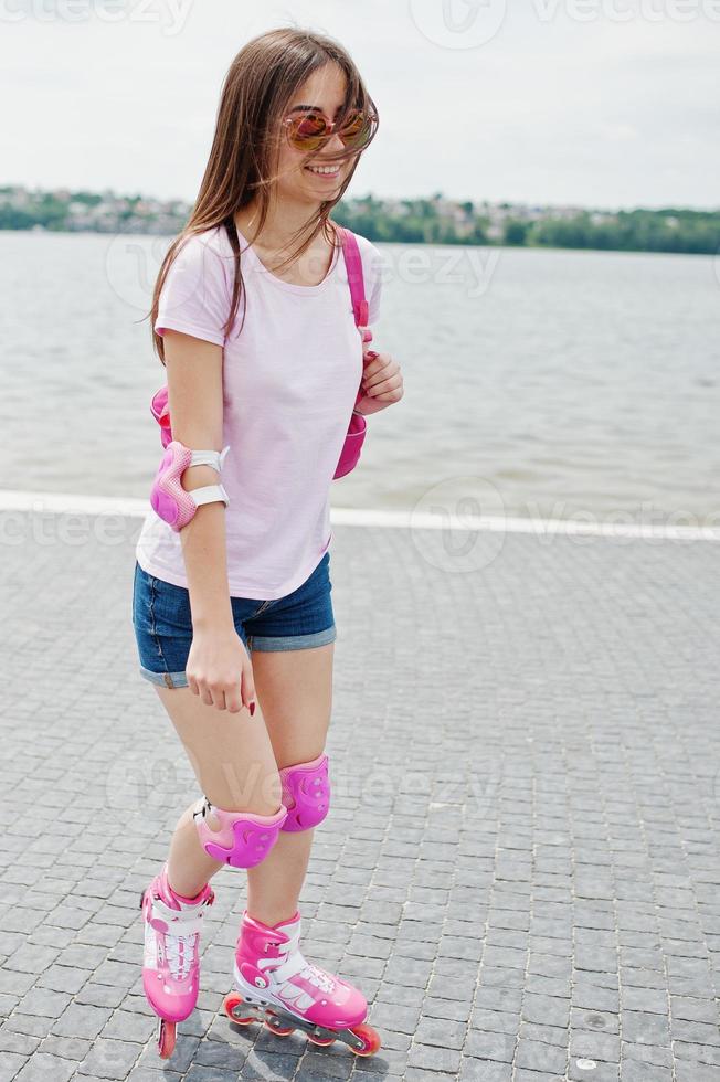 Porträt einer gut aussehenden jungen Frau in Freizeitkleidung, die auf dem Bürgersteig im Park Rollerblades fährt. foto
