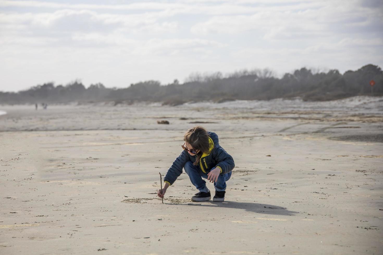 kleines Mädchen, das auf dem Sand am Strand zeichnet foto