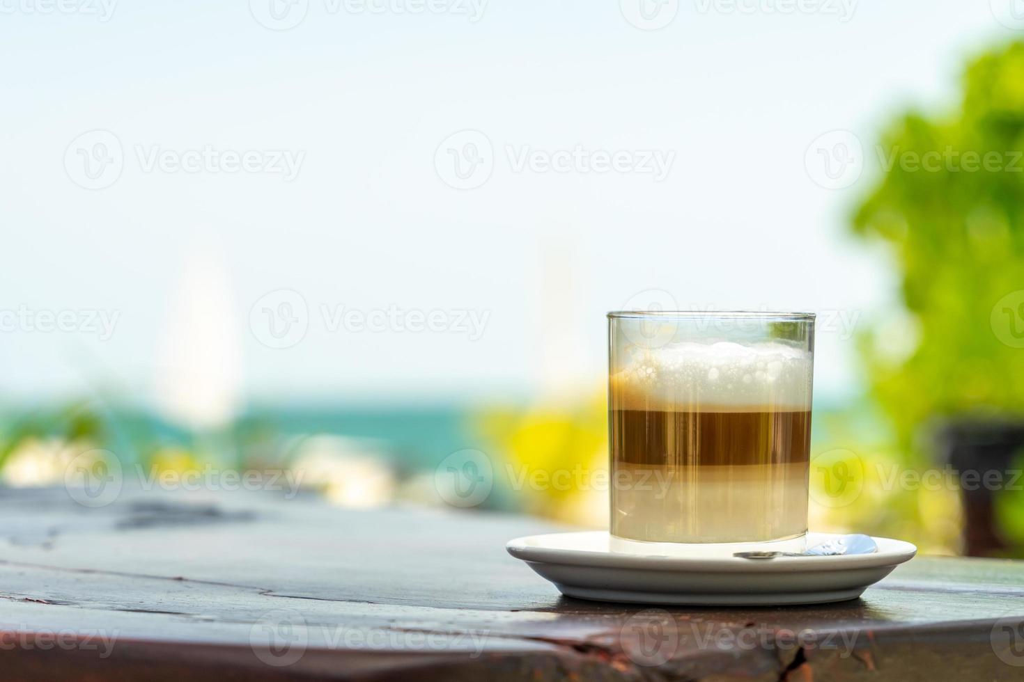 Latte-Kaffee im Glas auf Holztisch mit Meer- und Himmelshintergrund. foto