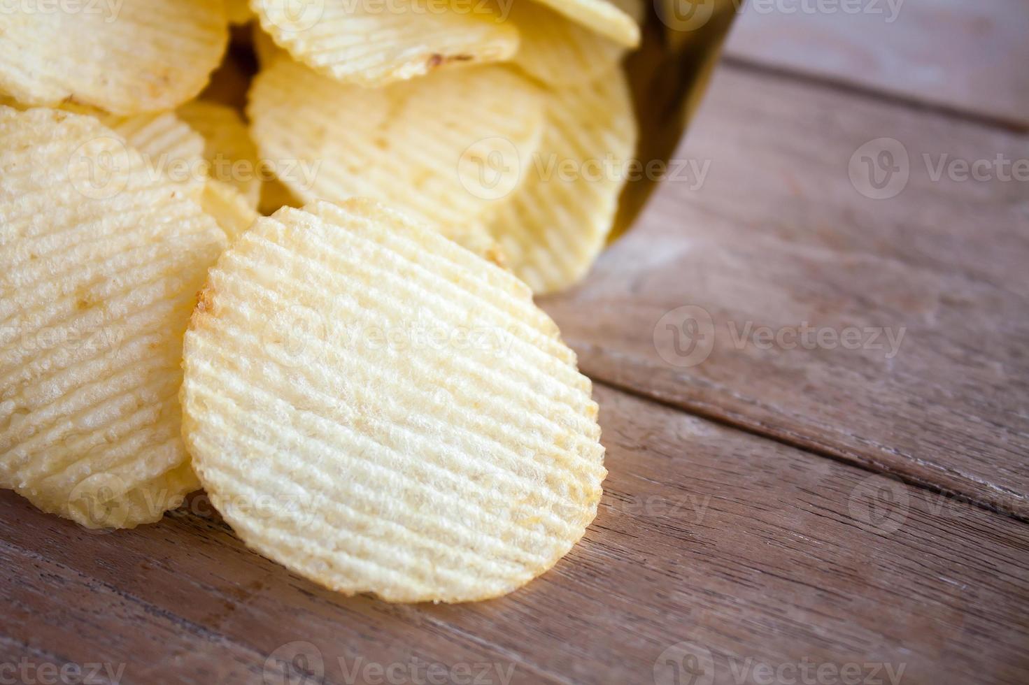 geöffnete Packung mit Kartoffelchips über Holztisch foto