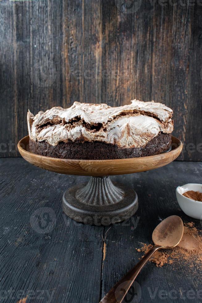 rund gebackener Brownie-Kuchen mit Baiser und Schokoladenstrudeln auf rustikalem Tortenständer foto