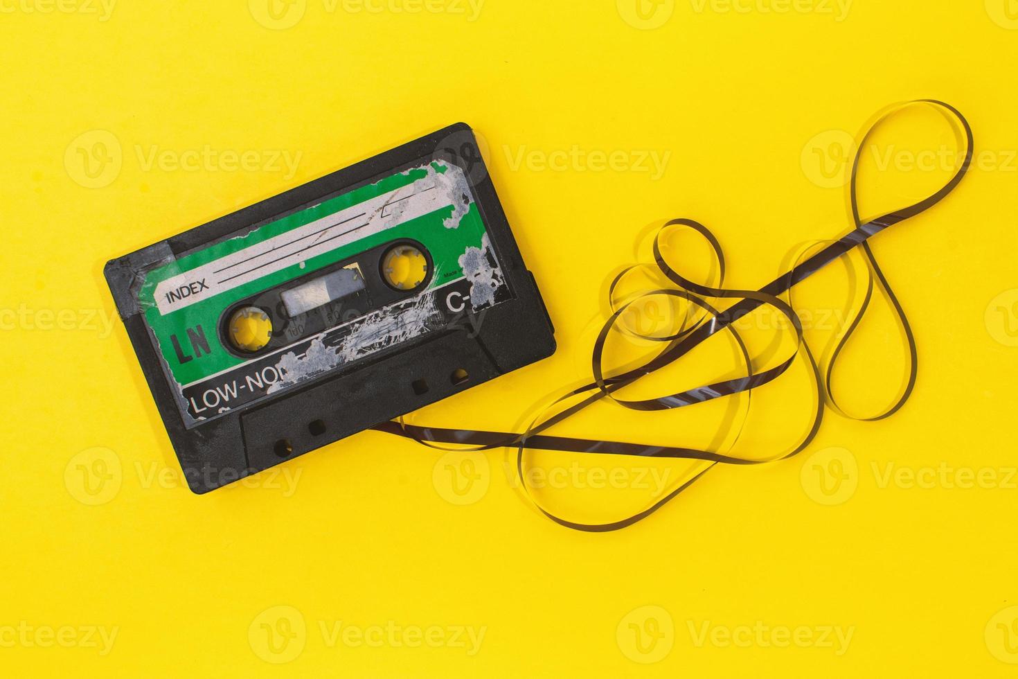 Altes Retro-Kassettenband mit Grunge-Etikett, umgeben von gezogenem Bandstapel auf gelbem Hintergrund, flach gelegt foto