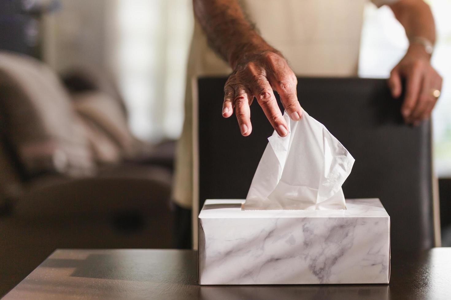 Hand des älteren Mannes, der Seidenpapier aus der Taschentuchbox auf dem Esstisch aufhebt. foto