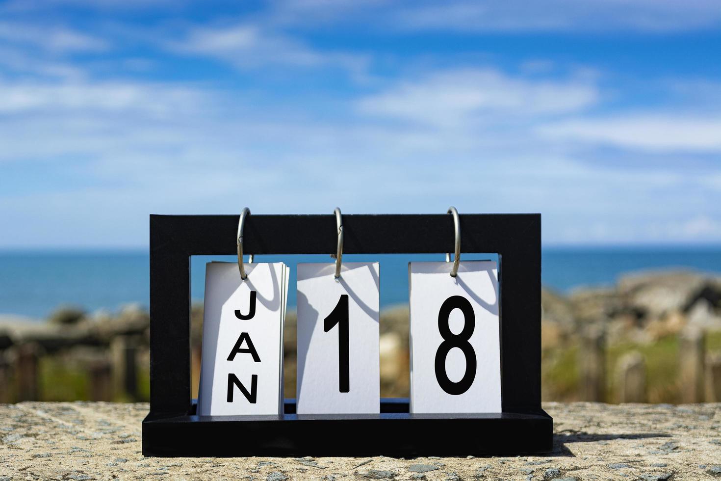 18. januar kalenderdatumstext auf holzrahmen mit unscharfem hintergrund des ozeans foto