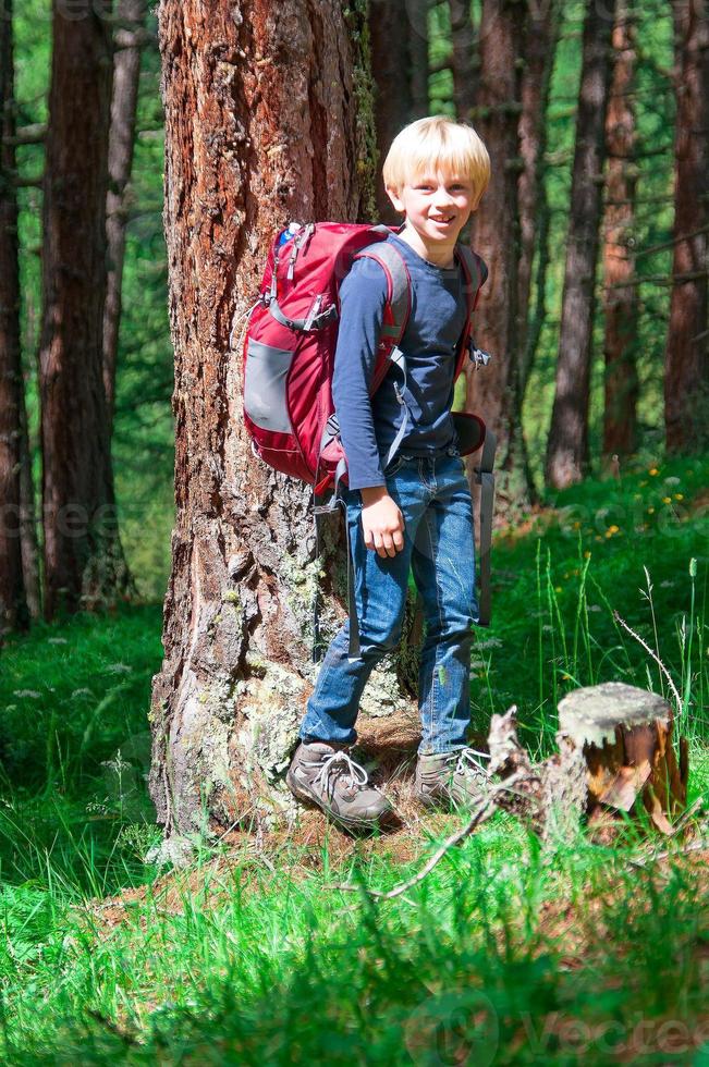 Blondes Kind, das Trekking zwischen den Bergwäldern praktiziert foto