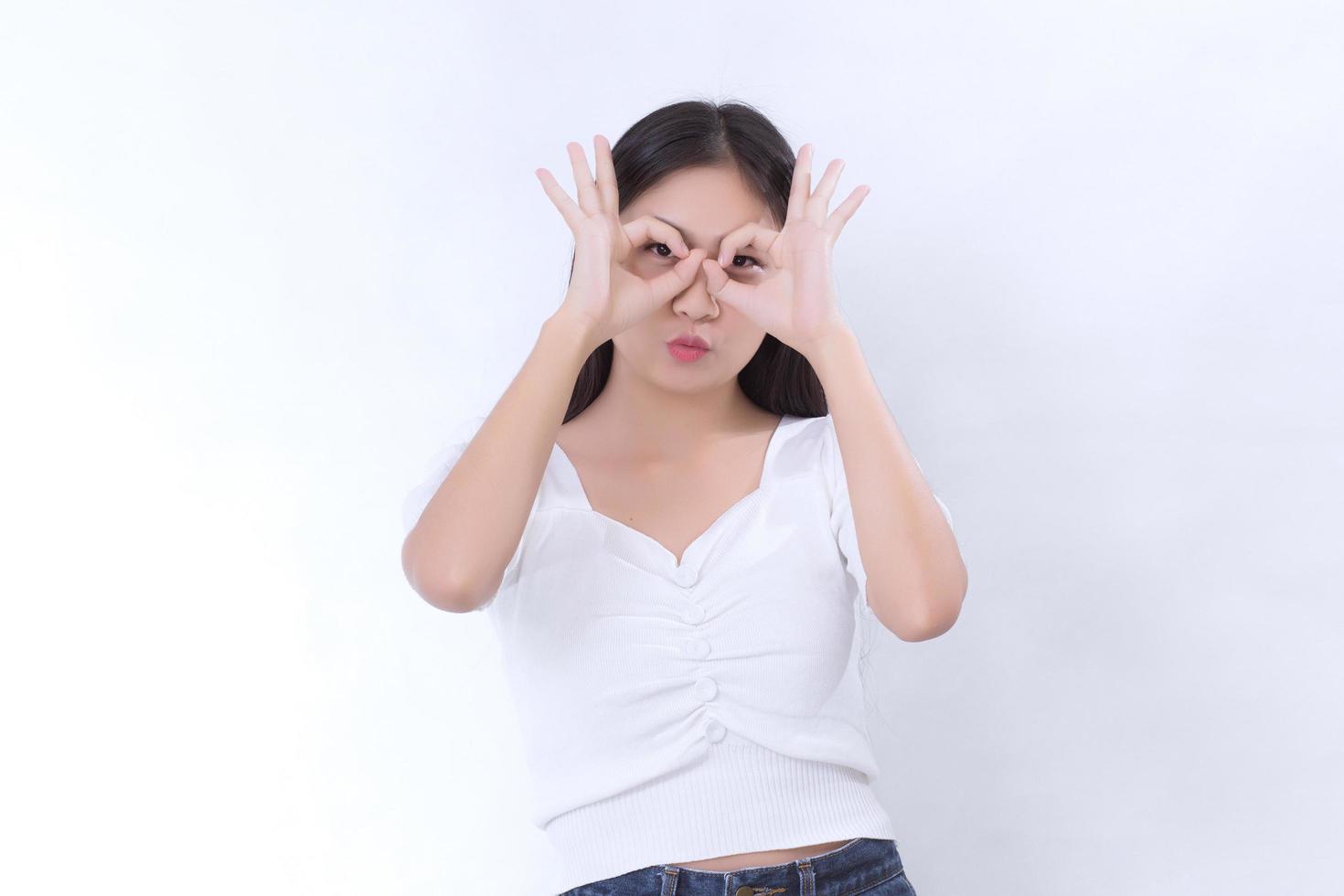 asiatische frau mit langen schwarzen haaren trägt weißes hemd und zeigt hand-okey-zeichen auf weißem hintergrund. foto