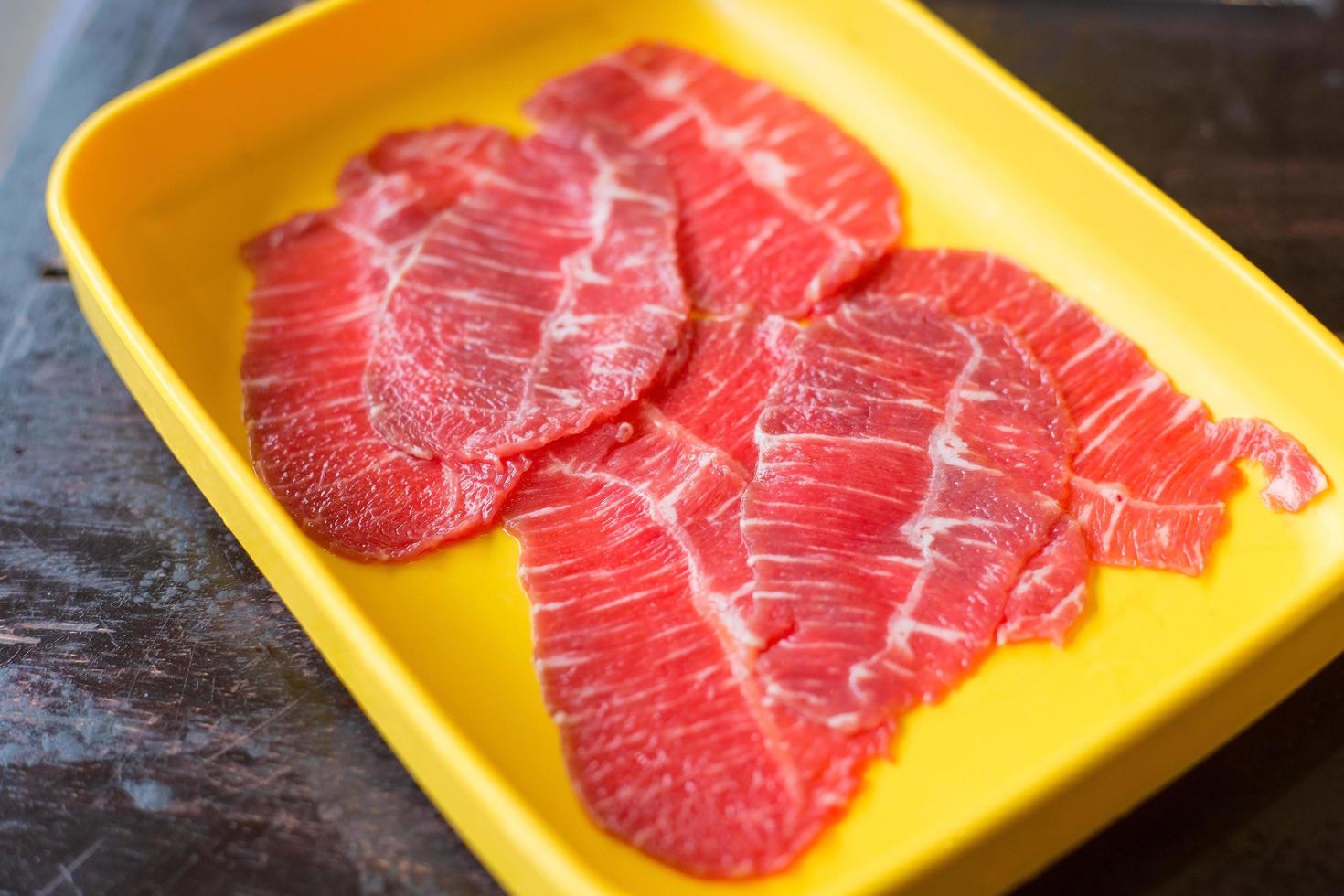 frisches Rindfleisch wurde roh in Scheiben geschnitten für das Restaurant Sukiyaki und Shabu oder Yakiniku serviert, das auf einen gelben Teller gestellt wurde. foto