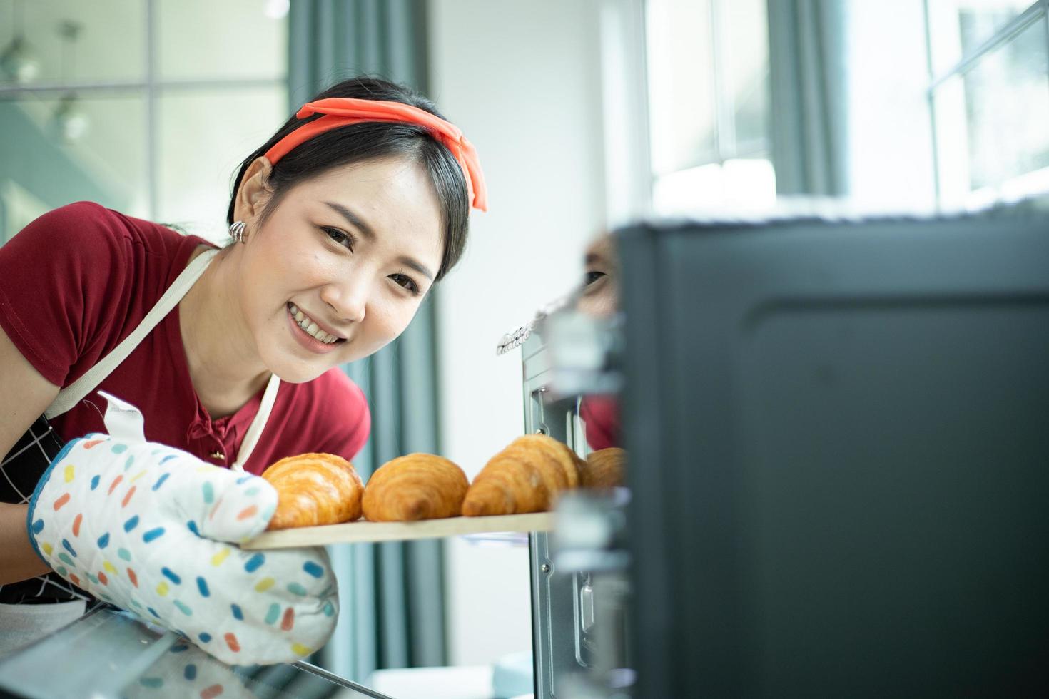 Eine glückliche junge Frau, die gebackene Croissants aus einem Ofen entfernt foto