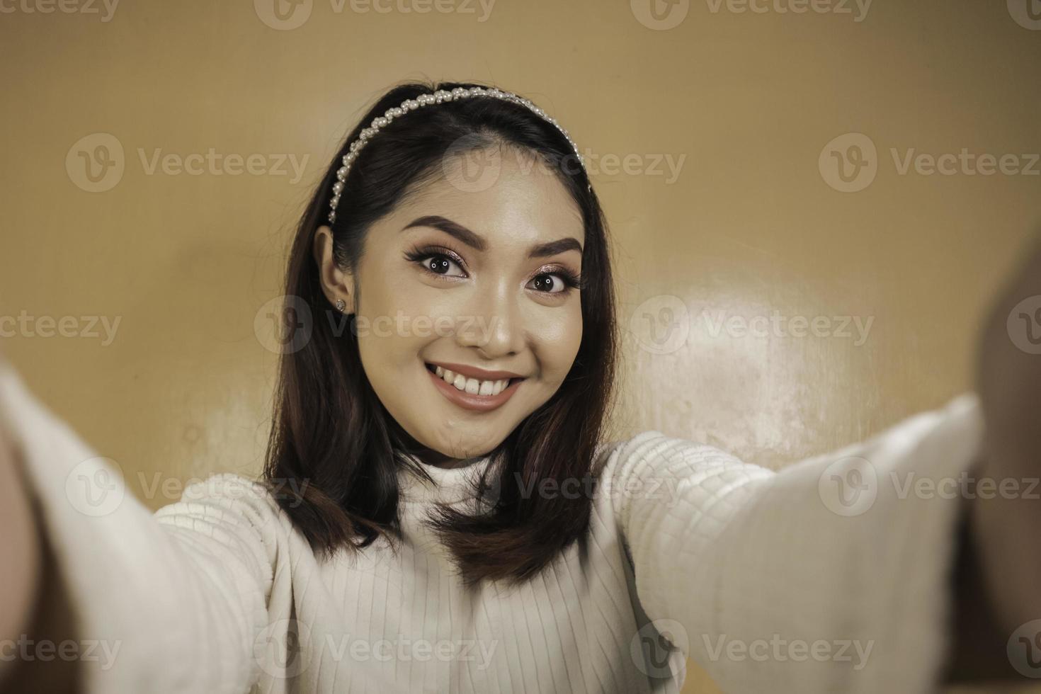 junge asiatin lächelt und macht selbstfotos mit ihrem handy. indonesische Frau auf orangefarbenem Hintergrund. foto