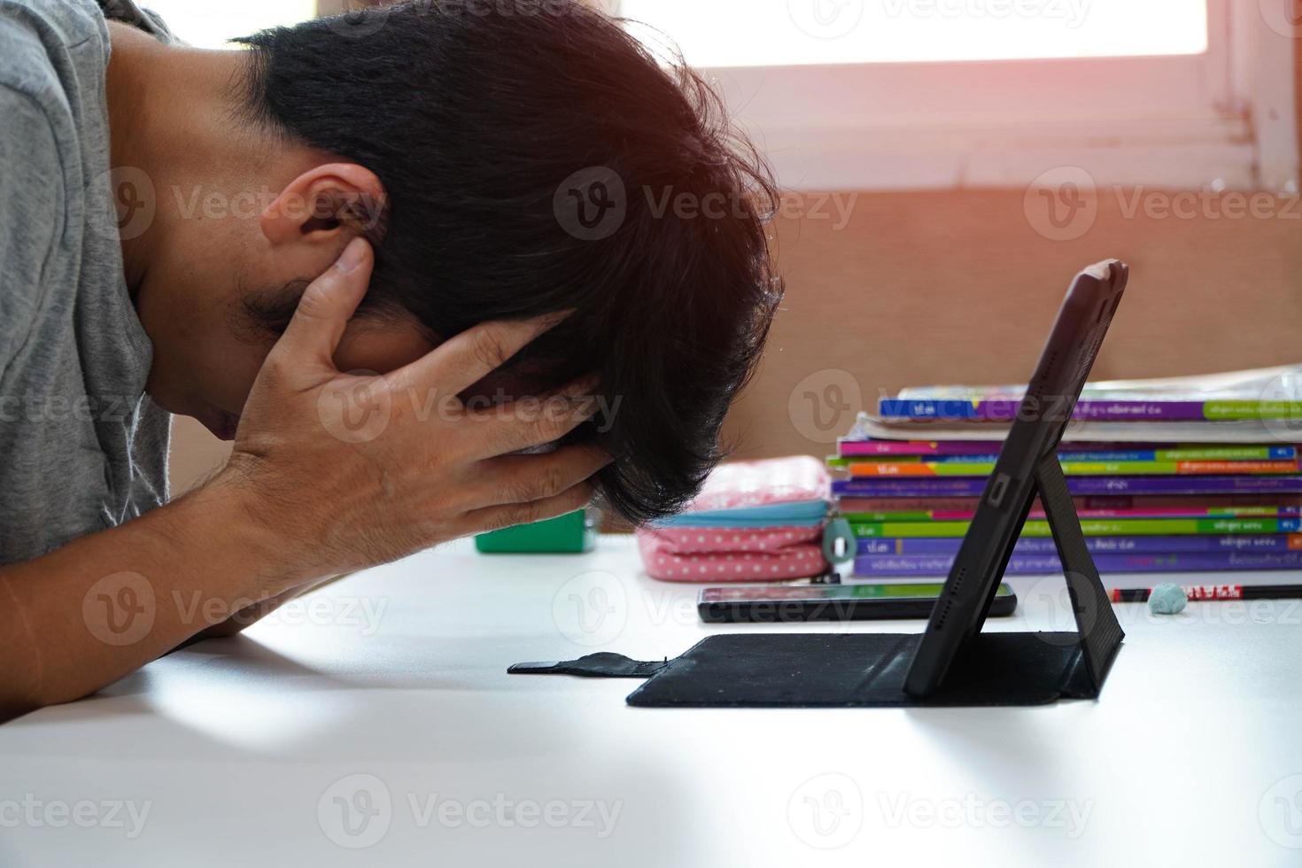 asiatische männer mit kopfschmerzen von der arbeit zu hause, man fühlt sich müde, gelangweilt und schläfrig auf dem tisch sitzend. er schaut auf den computer und denkt über den job im wohnzimmer zu hause nach, home office wegen der covid19-pandemie foto