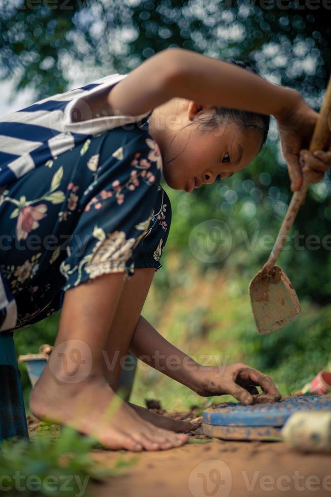 Ein kleines asiatisches Mädchen spielt tagsüber in seinem Haus mit Erde in der Natur. foto