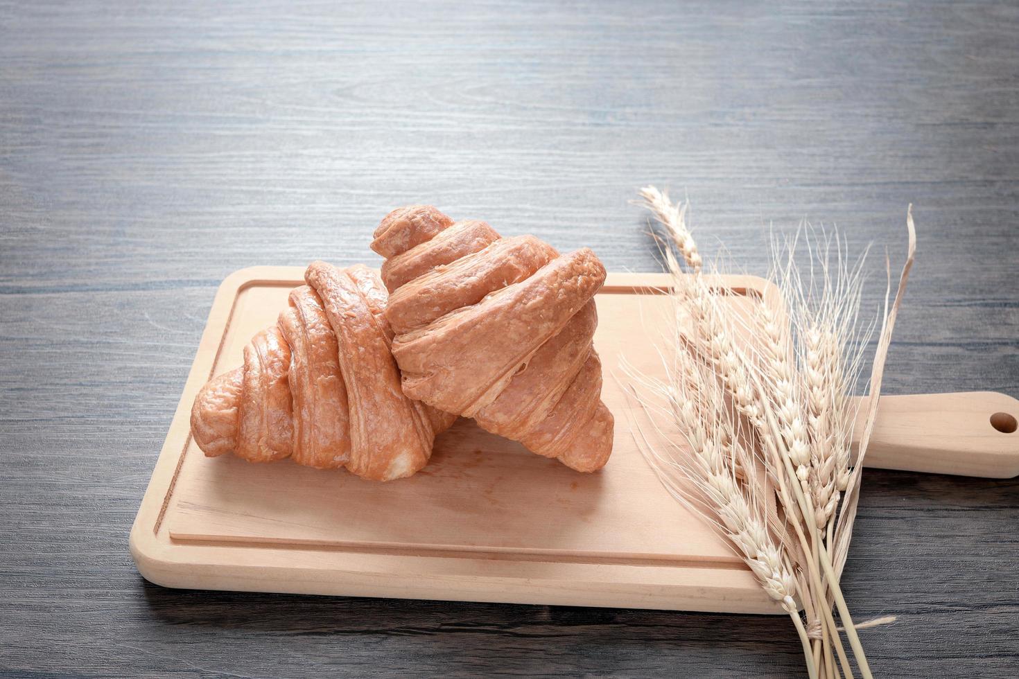 Zwei frisch gebackene leckere Croissants mit Ährchen auf Holzschneidebrett, Essen auf dem Frühstückstisch foto