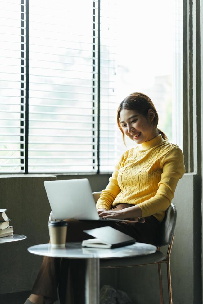 porträt einer schönen asiatischen frau, die im sommer drinnen im café-restaurant sitzt, mit intelligenter drahtloser technologie, computer-laptop und smartphone, entspannende kaffeepause im café-restaurant. foto