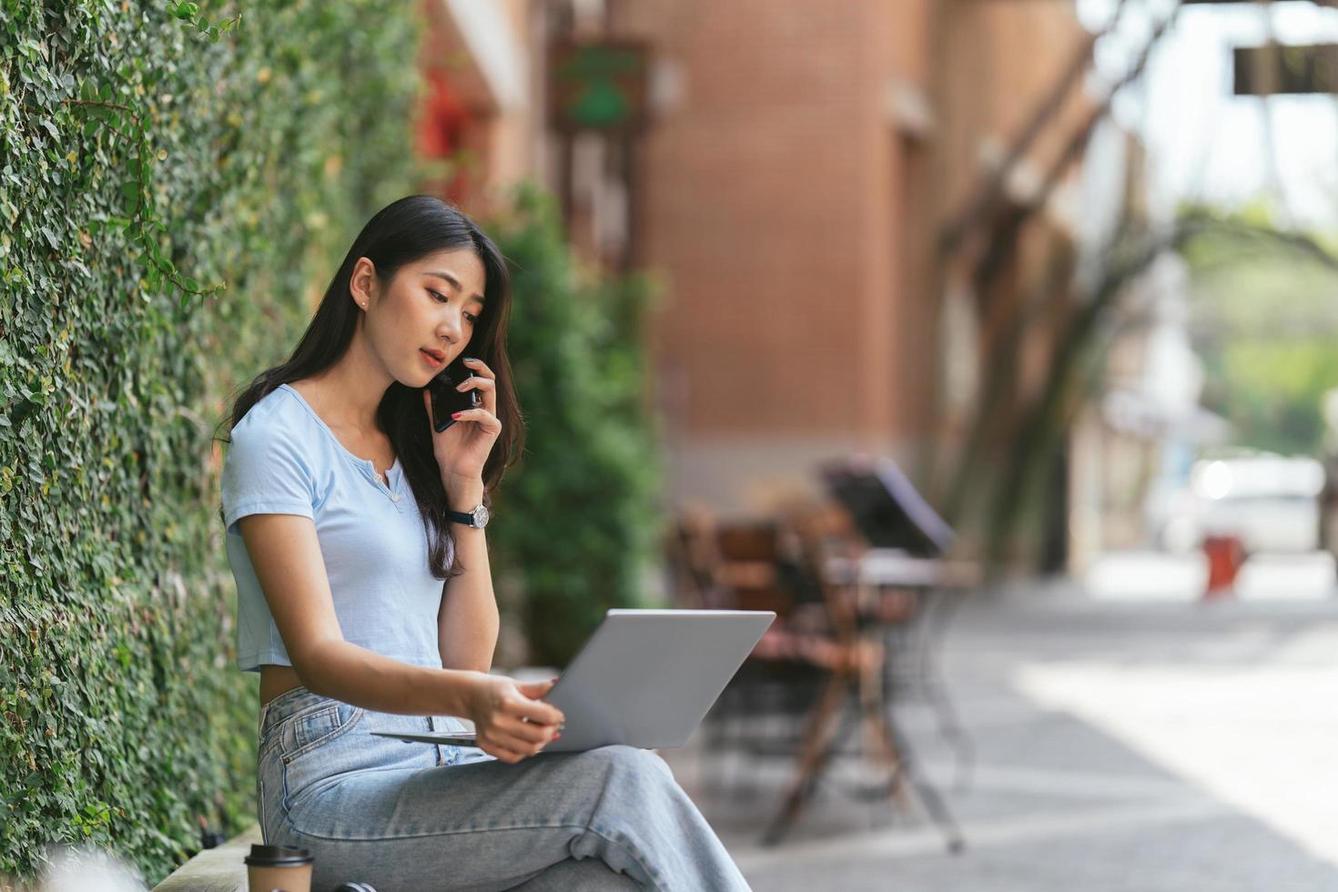 porträt einer schönen asiatischen frau, die im sommer draußen sitzt, mit intelligenter drahtloser technologie, computer-laptop und smartphone, entspannende kaffeepause im café-restaurant. foto