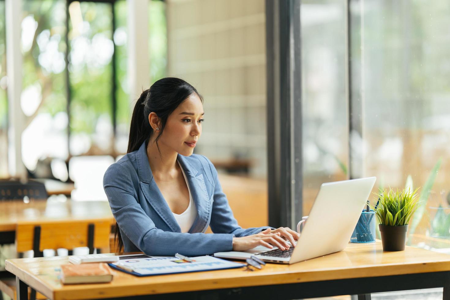 Porträt einer asiatischen jungen Frau, die im Büro an Laptop und Finanzbericht arbeitet. foto