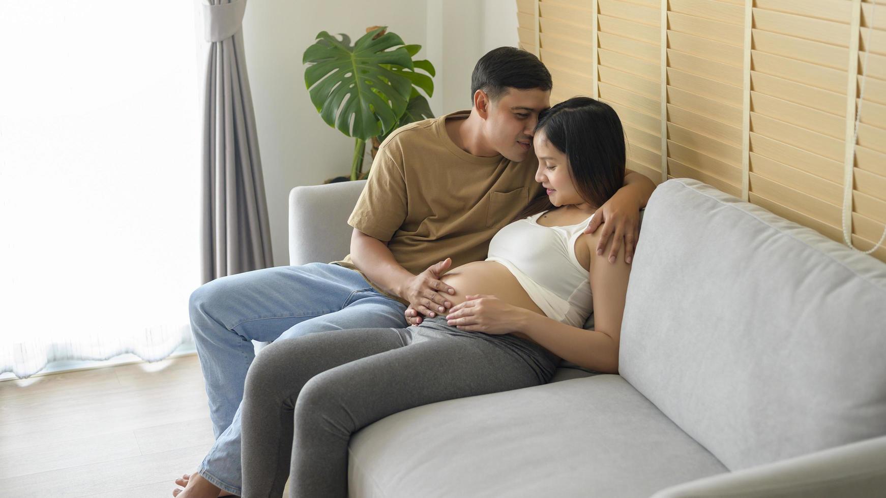 junge schwangere frau mit ehemann, die zu hause ein baby umarmt und erwartet foto