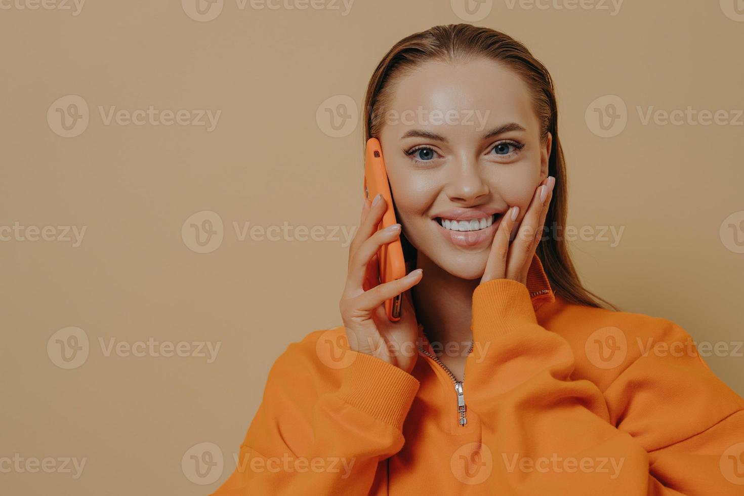 glückliche aufgeregte frau, die am telefon spricht, gute nachrichten über handy hört, isoliert über beiger wand foto